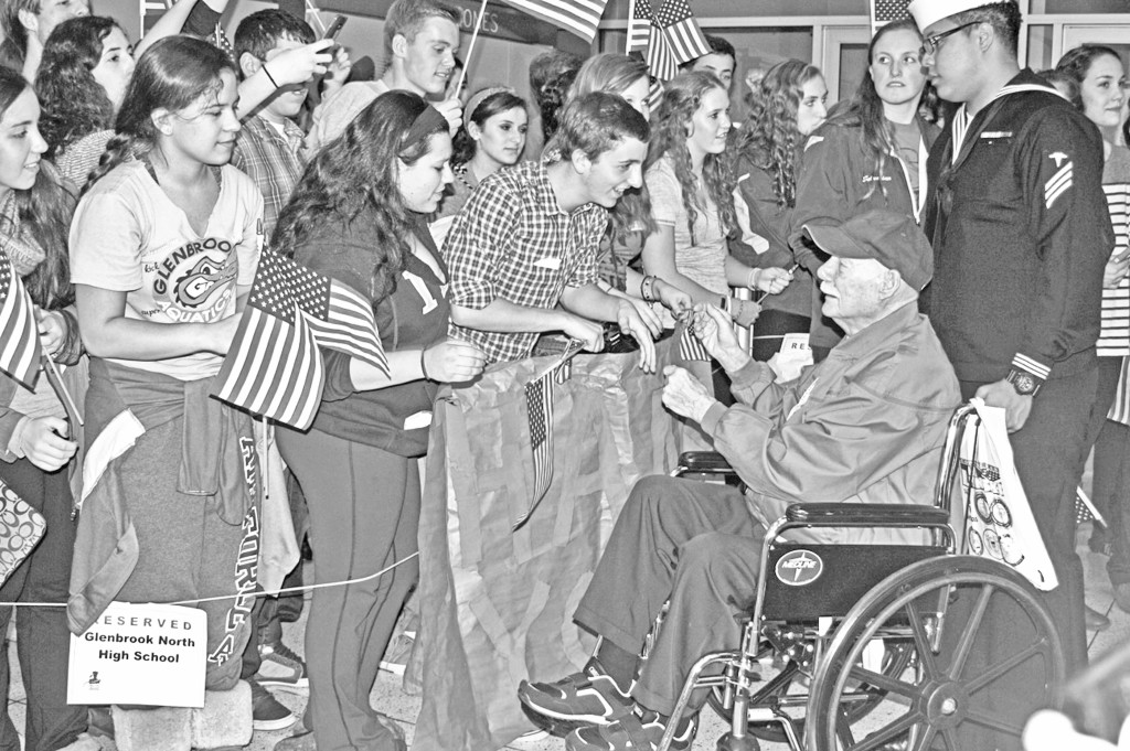 Junior Jonah Blocker shakes hands with a Word War II veteran while other students hold flags and cheer. The veterans were returning from Washington D.C. where they were recognized in the Honor Flight ceremony for their commitment and service. Photos by Lauren Sulkowski.