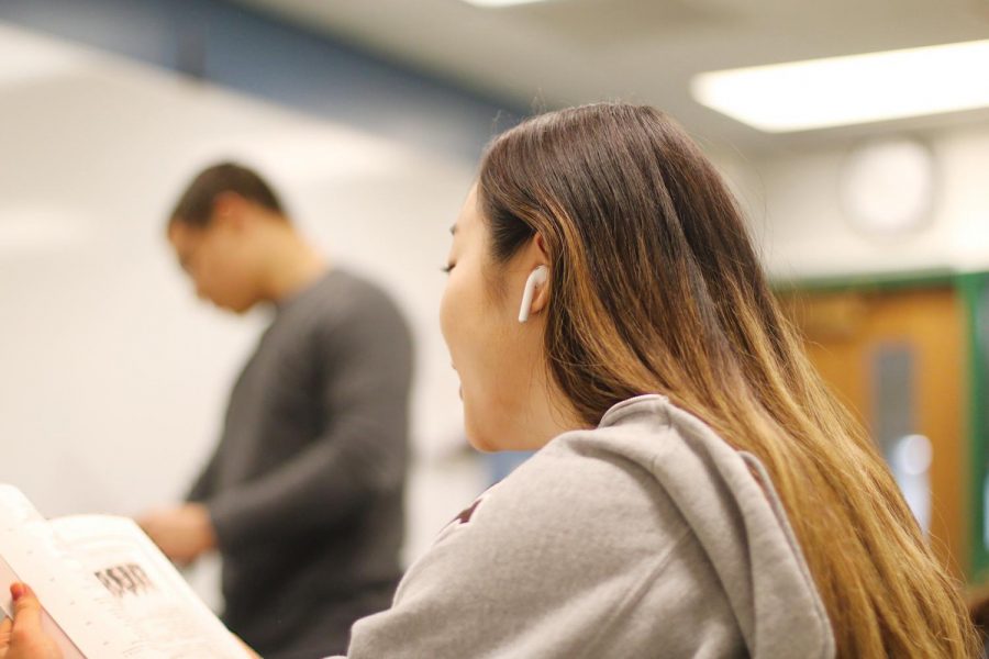 A student has her AirPods in as she reads a book during class. Student use of AirPods in classrooms has raised concern from teachers over the potential impact on students’ learning environments. Photo by Sarah Boeke