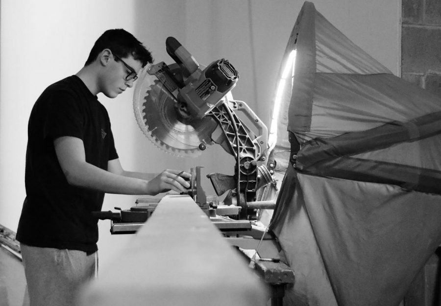 Sophomore Ben Earle, stage crew board member, cuts wooden planks with a circular saw to make the platform for the variety show. Photo by Maya Fridman