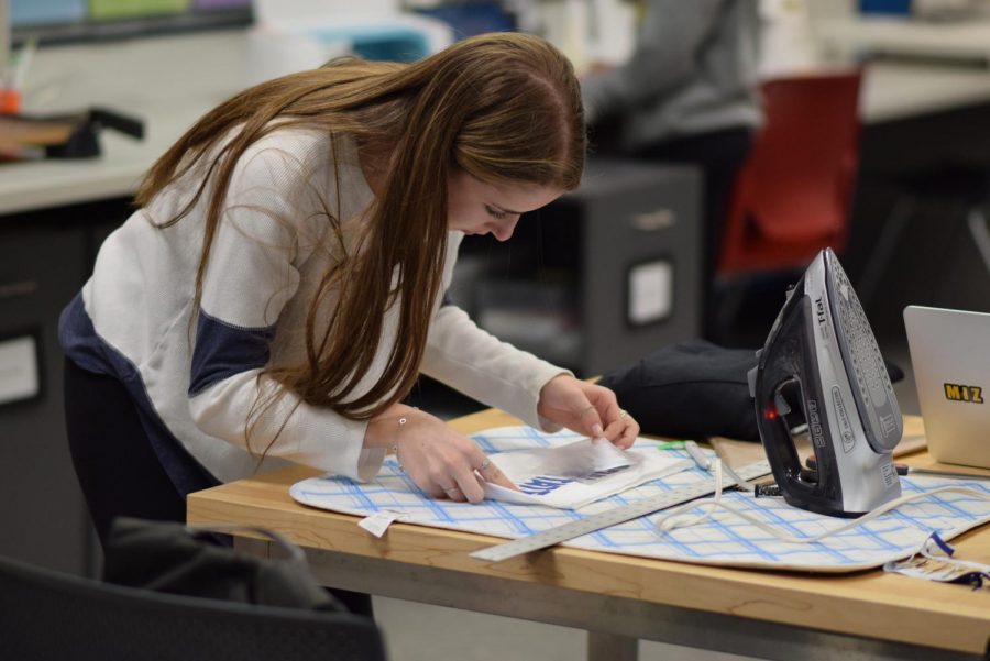 Senior Sarah Glass leans down as she works on a piece of customized apparel. In 2019, she and seniors Julia Foster and Sophie Rogoff co-founded Hardcore College, an Instagram account that sells customized clothing.