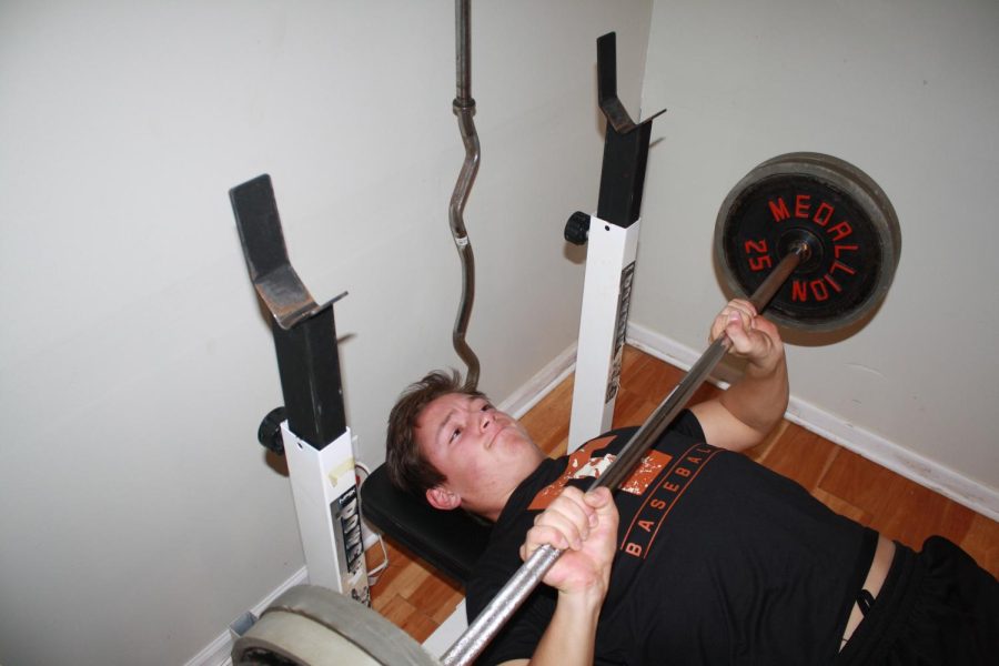 Junior NJ Gott reps out bench presses in his basement gym. Earlier this school year, Gott employed a bulking and cutting diet in order to increase muscle mass. Photo by Kate Leverenz