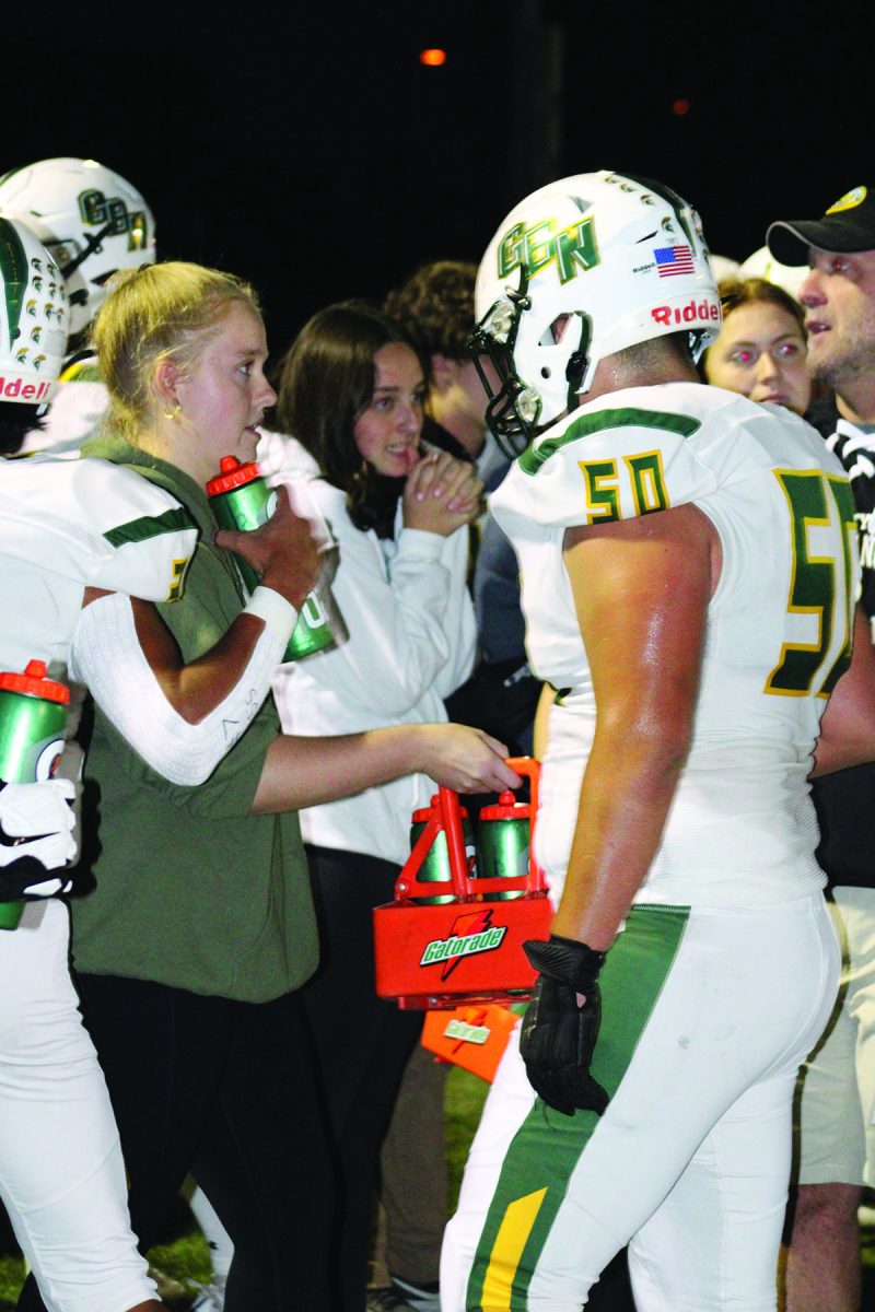 Senior Olivia Stasieluk offers water to football players during halftime at an away game against Buffalo Grove on Sept. 14. Student athletic trainers can travel on team buses or by themselves to aid athletes at away games. Photo by Lara White