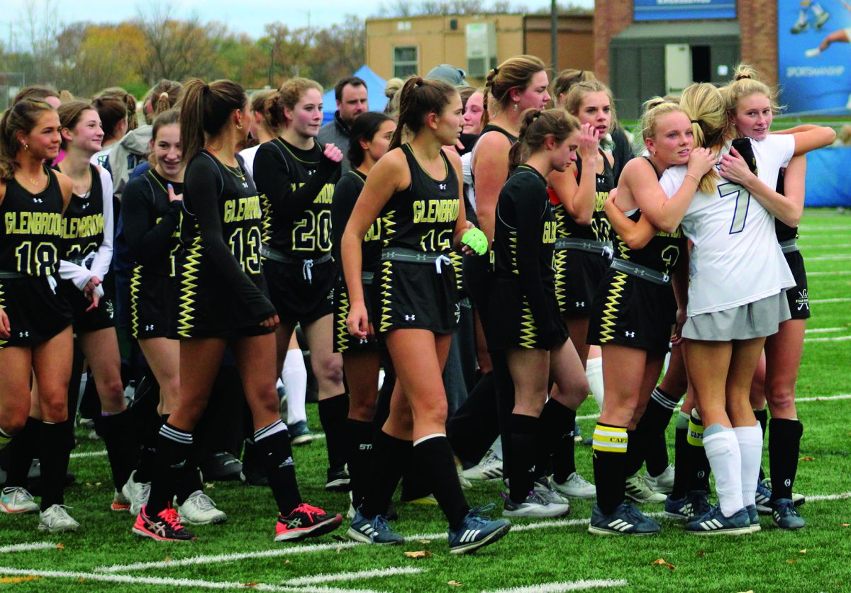 The Glenbrook field hockey team follows junior Reese Anetsberger (left) and senior Madison Beach as they embrace a New Trier opponent at the state final on Oct. 28. Photo by Lara White