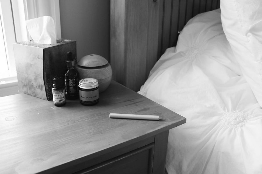 An essential oil vape lies on a nightstand with essential oils and a  diffuser, as essential oils are marketed to help people sleep.