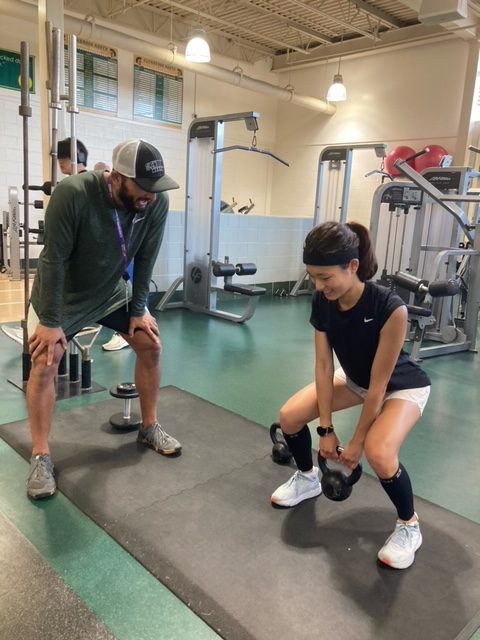 During a lift for cross country, Jayson Patel, head strength & conditioning coach (left) assists senior Willow Kim with her squatting form. Patel has worked with P.E. classes and  sports teams both in and out of season. Photo by Nora Skiest