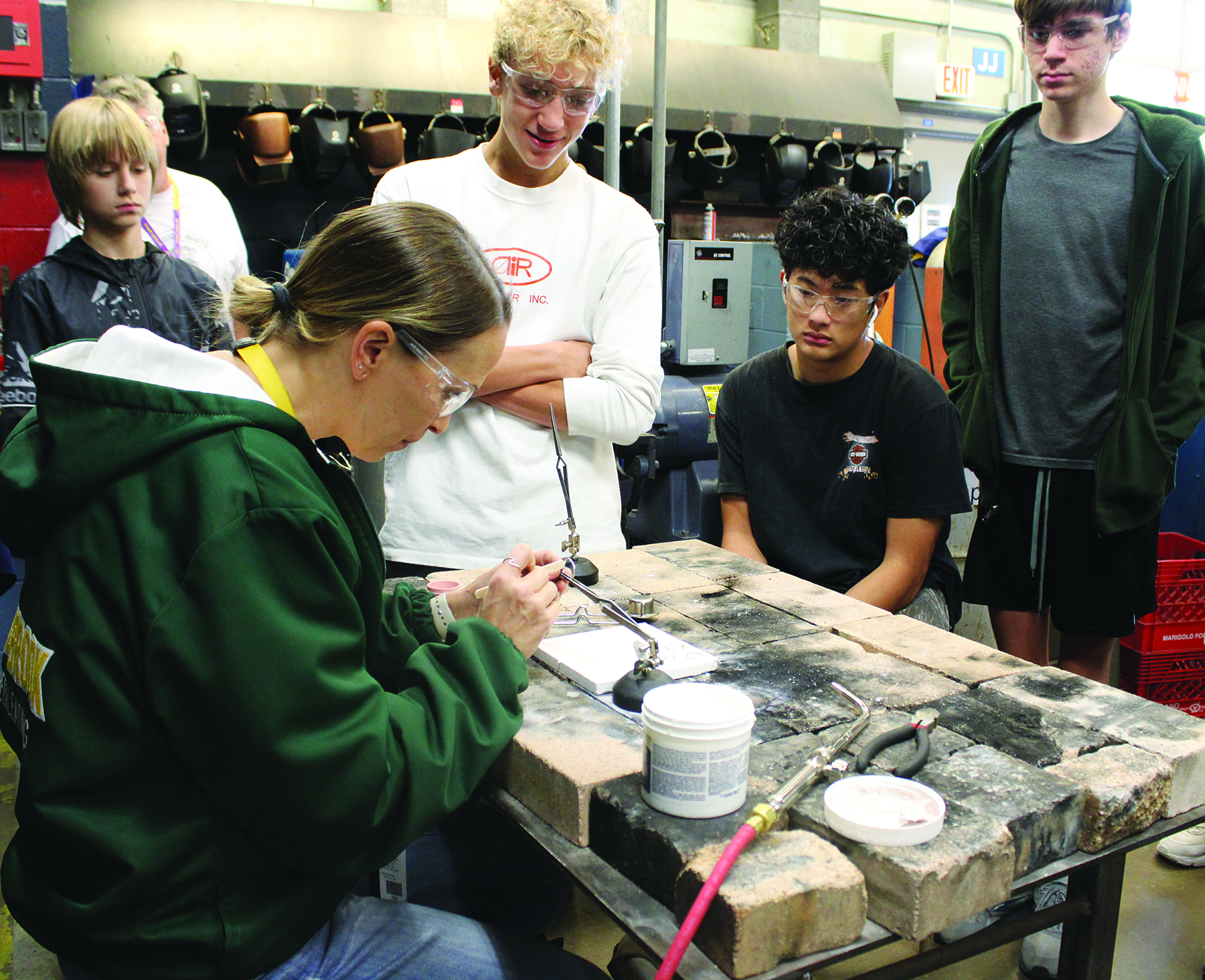 Metals Design teacher Christina Rose (left) demonstrates how to solder rings together. Engineering skills and jewelry-making are taught through hands-on projects in the revised curriculum.