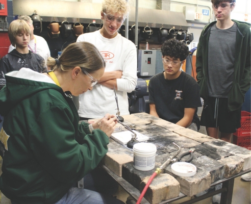 Metal Design teacher Christina Rose (left) demonstrates how to solder rings together. Engineering skills and jewelry-making are taught through hands-on projects in the revised curriculum.