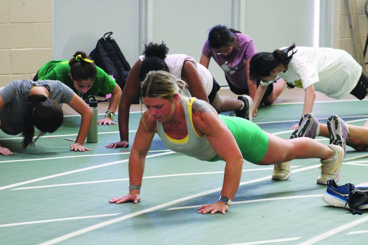 Kelly McClearn, girls cross country coach (front), leads the team through push-ups at practice on Sept. 20. McClearn also runs with the team at practice in addition to her CrossFit training. 